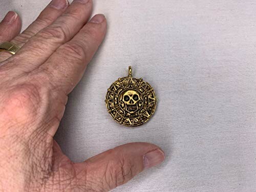 Hand near a golden skull medallion on a flat surface